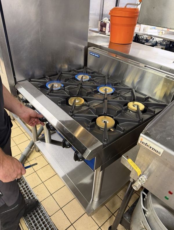 Six-burner gas range with all burners lit after a repair
